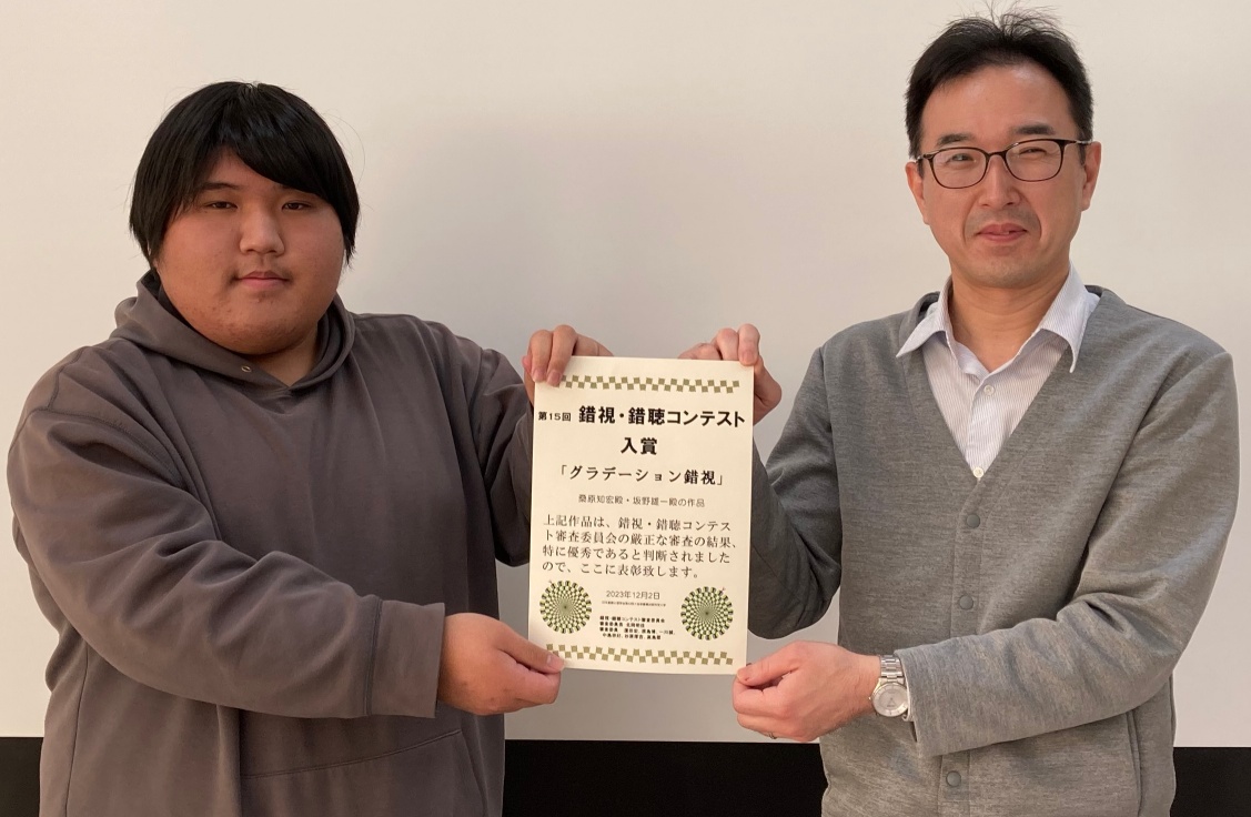 桑原知宏君と坂野雄一が錯視・錯聴コンテスト入賞の賞状を一緒に持っている写真